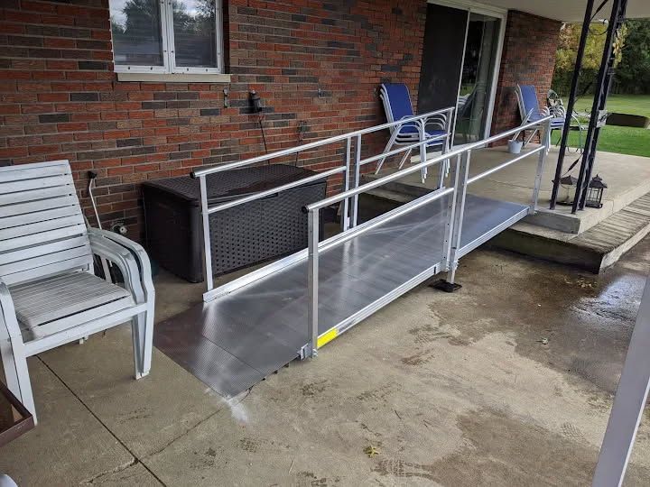 Aluminum ramp providing access to a porch with brick wall and patio furniture.