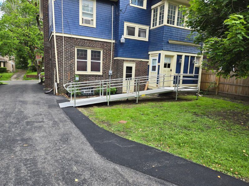 Blue building with a metal ramp for accessibility, on a grassy lawn next to a paved driveway.