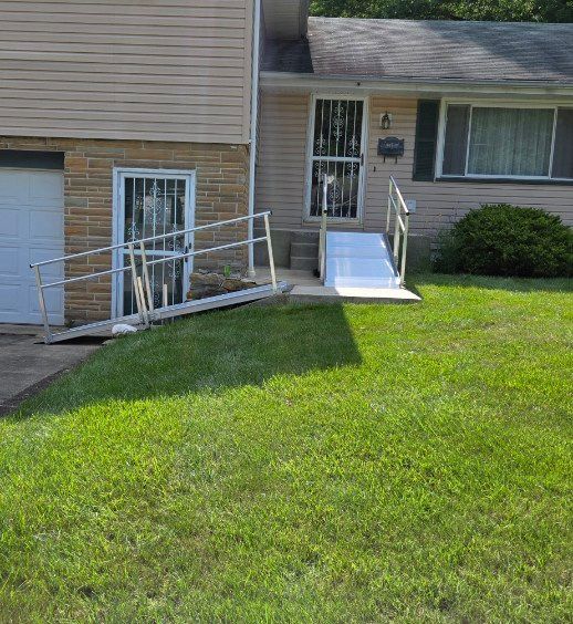 A house with two ramps: one to the door, one to a side door. Both have railings; a green lawn is in the front.
