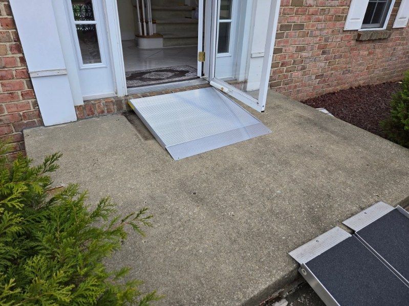 A concrete porch with a metal ramp leading to a front door of a brick house; a smaller ramp is on the right.