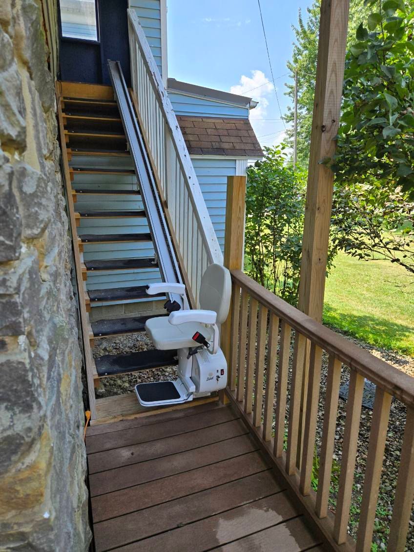 Stair lift on outdoor wooden staircase, providing access to a doorway. Sunny, daytime.