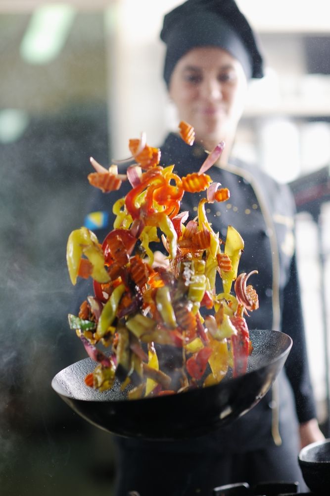 Chef Tossing Colorful Vegetables in a Wok, Kitchen Setting — Chefs2Go in Airlie Beach, QLD