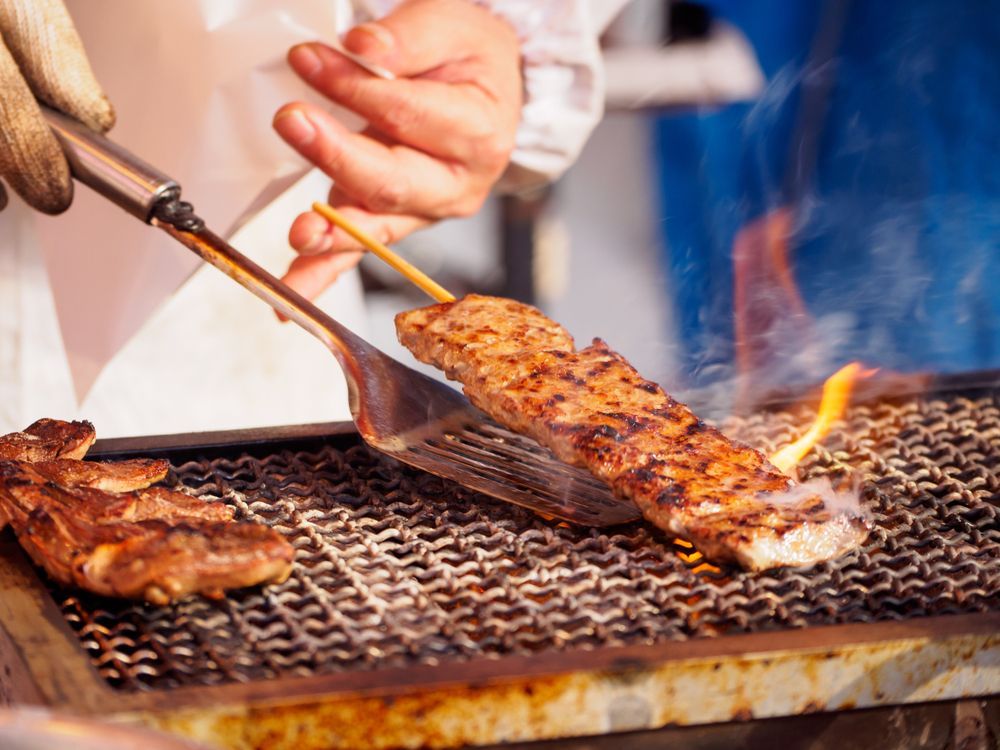 Grilling Meat on a Metal Grate With Flames Visible. a Hand Uses a Spatula to Flip a Skewer — Chefs2Go in Townsville, QLD
