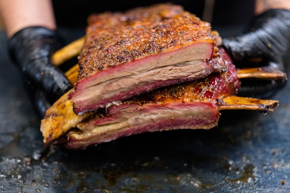 Sliced Smoked Beef Ribs With a Visible Pink Smoke Ring, Held by Gloved Hands — Chefs2Go in Townsville, QLD