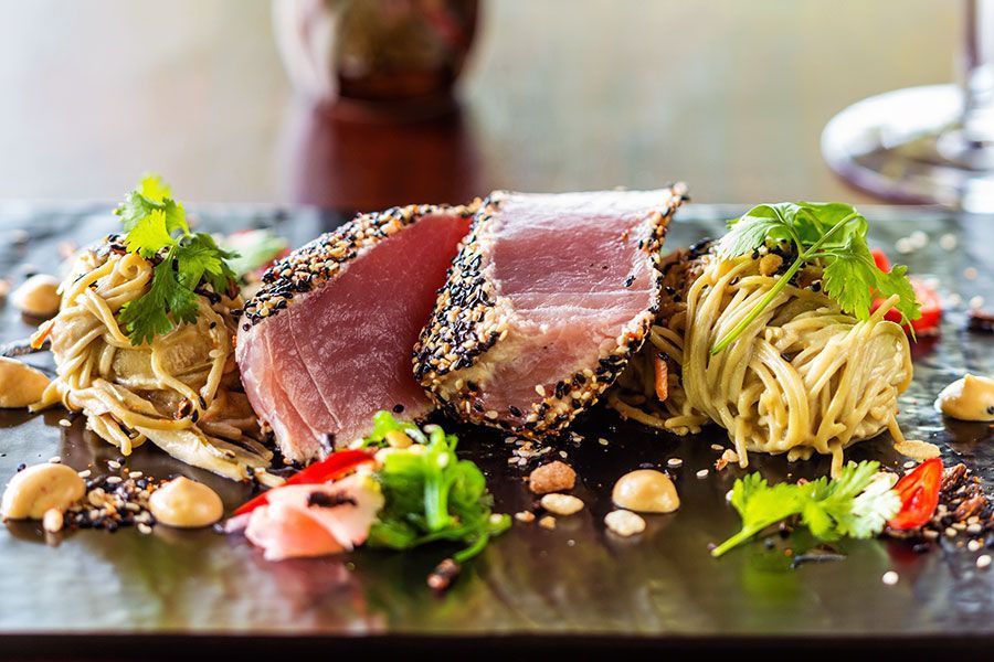 Seared Tuna With Sesame Seeds, Served With Noodles, Nuts, and Greens on a Black Plate — Chefs2Go in Sunshine Coast, QLD