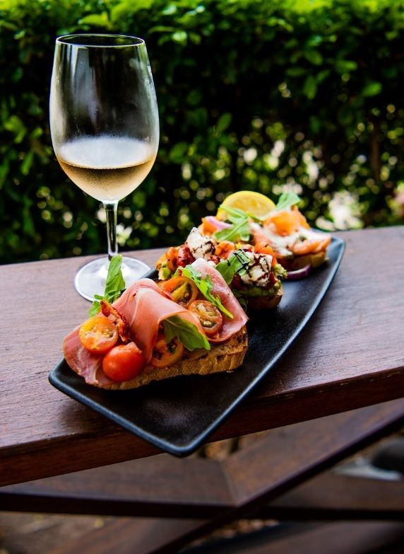 Wine Glass Beside a Tray of Gourmet Bread With Various Toppings — Chefs2Go in Woodwark, QLD