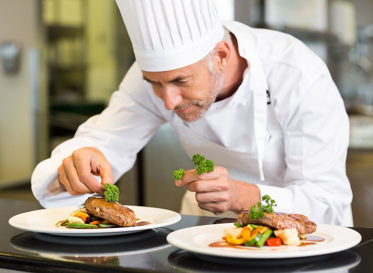 Chef Garnishes Plates of Food With Parsley in a Restaurant Kitchen — Chefs2Go in Woodwark, QLD