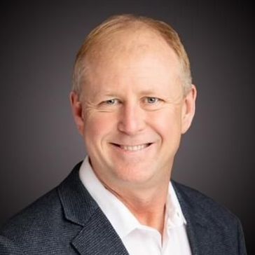 A man in a suit and white shirt is smiling for the camera.