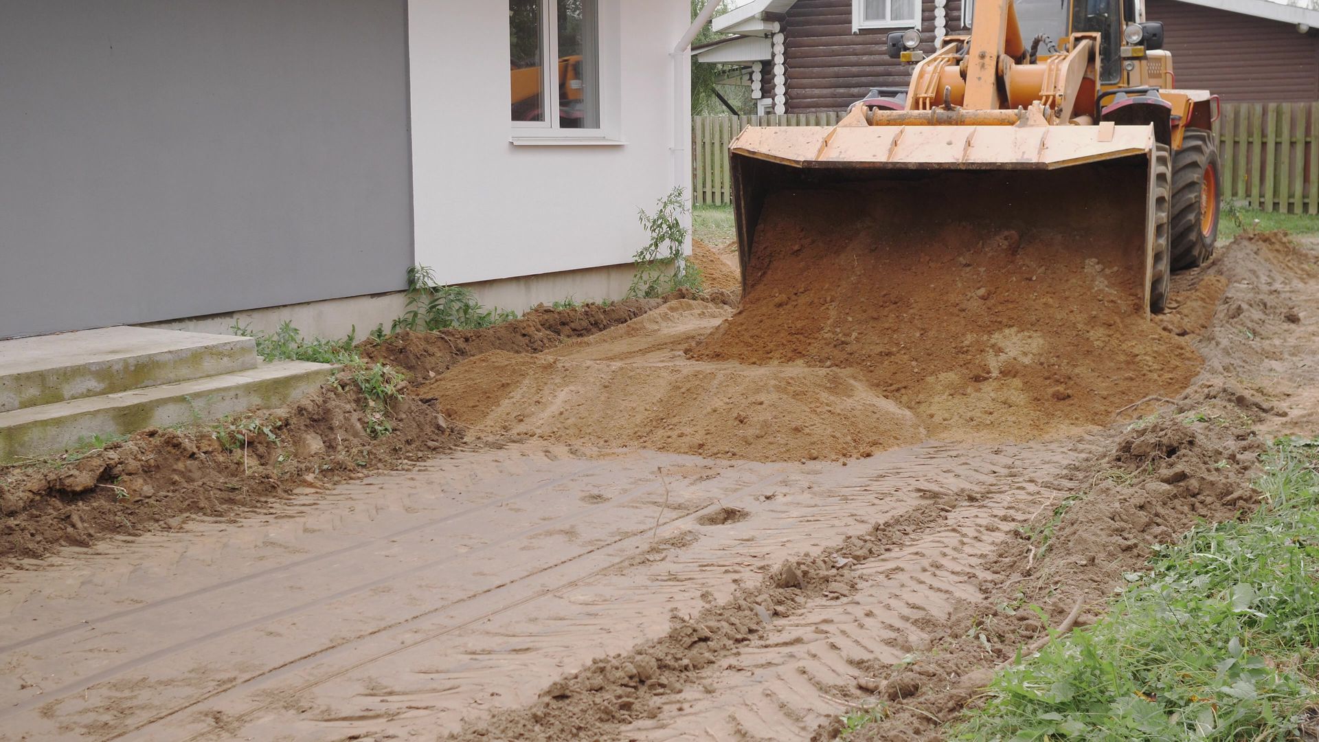 Front loader dumping dirt near a house with steps. Muddy ground.