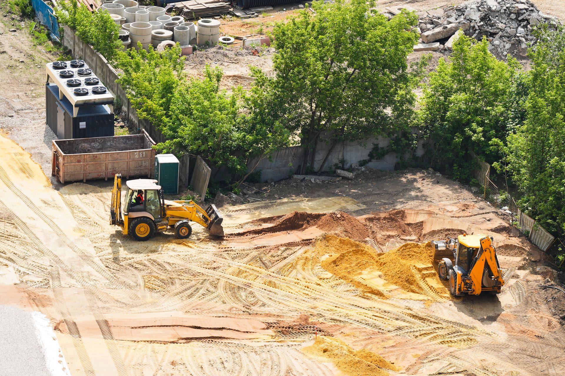 Construction site with two yellow backhoe loaders working on the dirt ground.