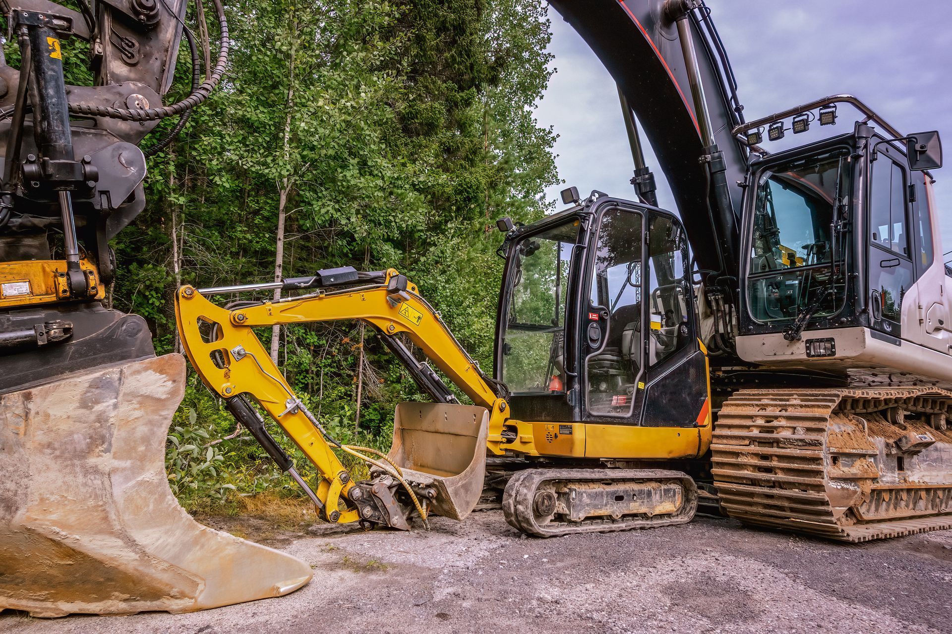 Yellow and black excavator machine parked on gravel, with bucket.