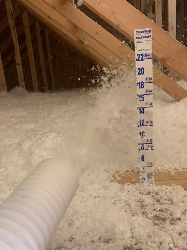 A measuring stick is being used to measure the amount of insulation in an attic.