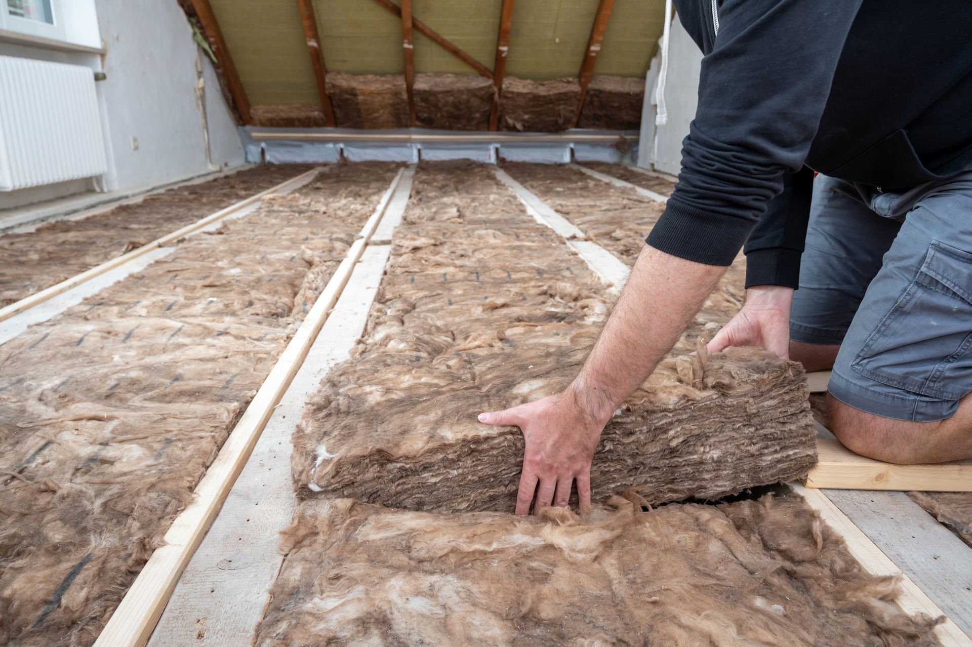 A man is laying insulation on the floor of a house.
