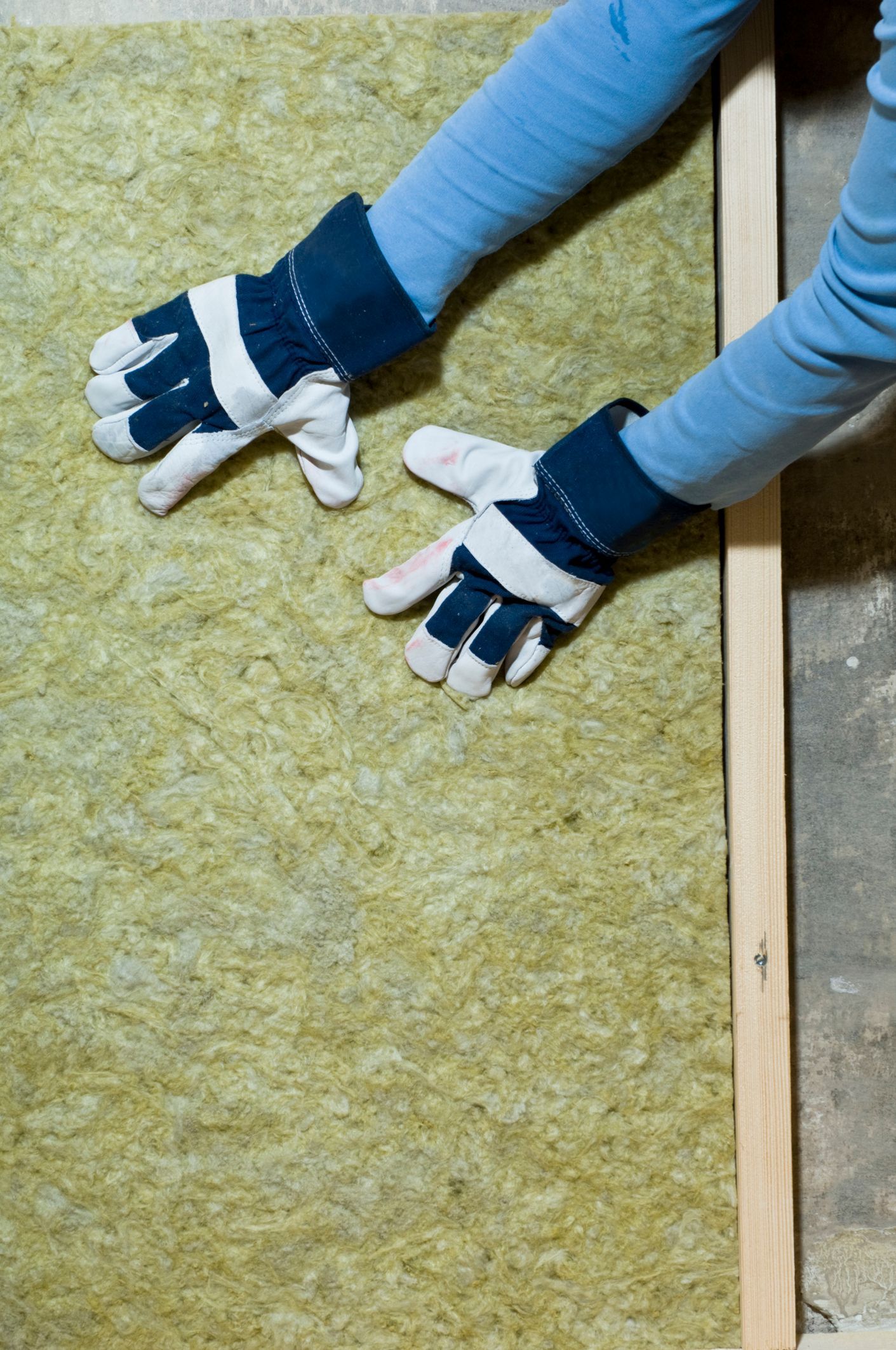 A man is measuring a piece of insulation with a tape measure.