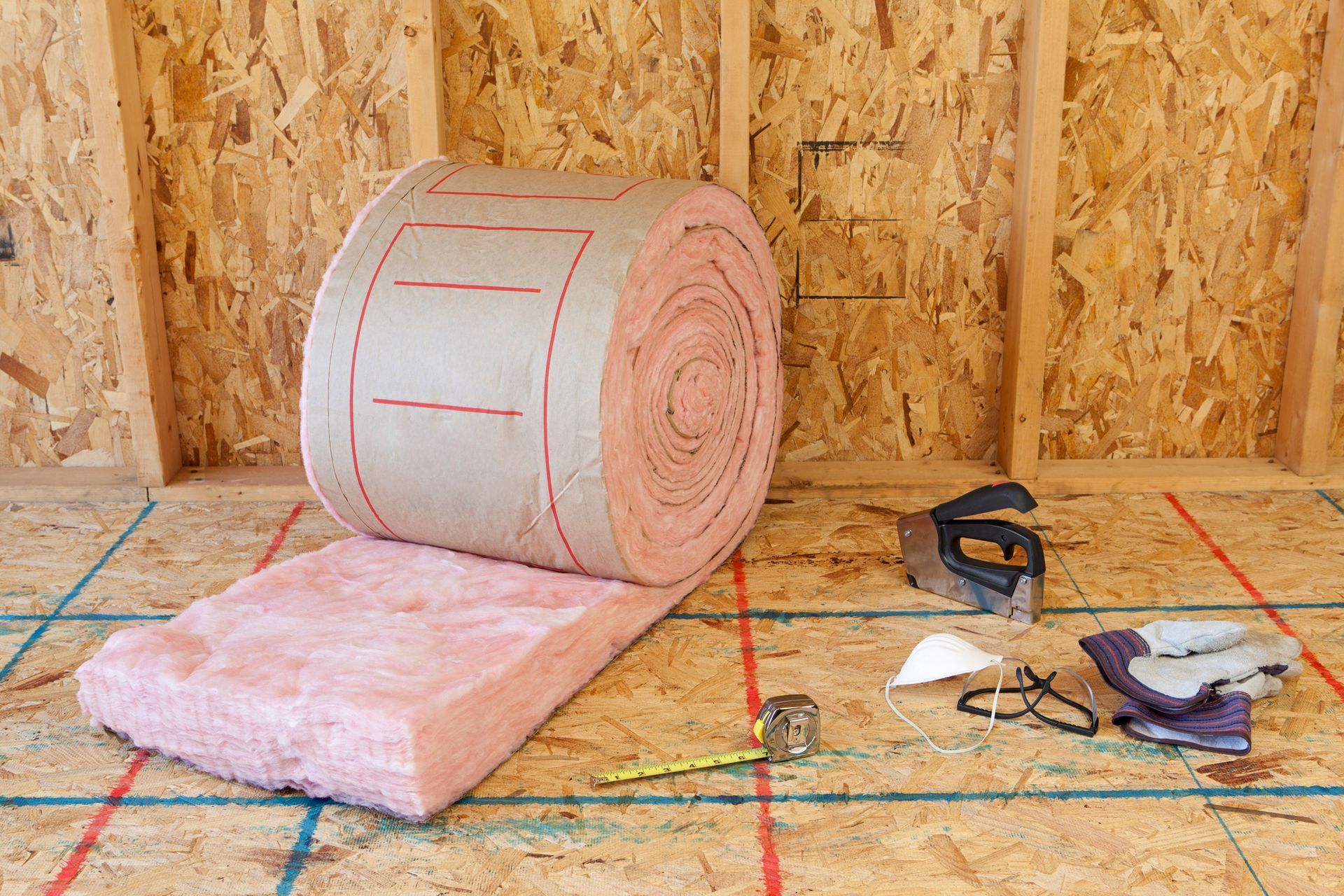 A wall with pink insulation on it and tools on the floor.