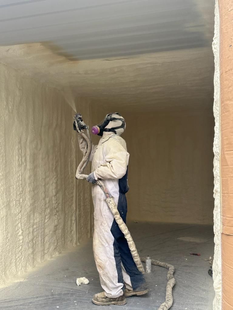 A man is spraying foam on a wall in a room.