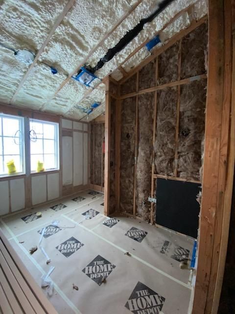 A man is standing on a ladder insulating a wall.