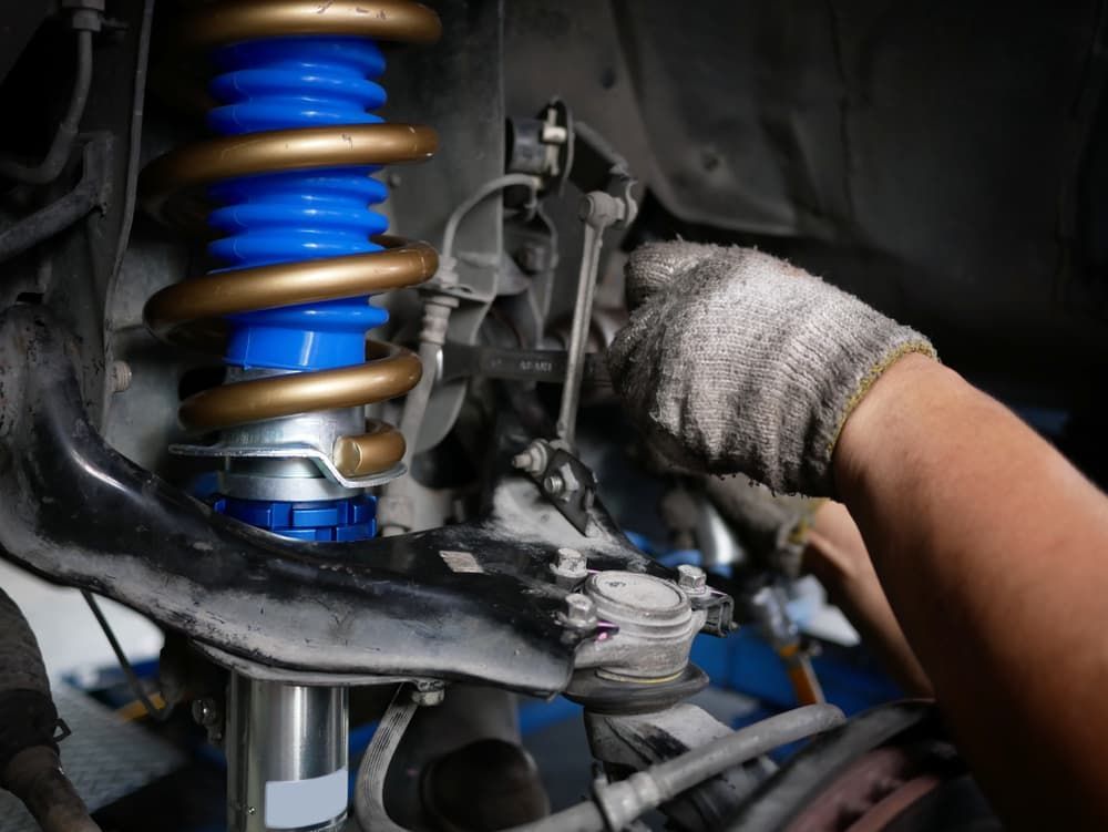 A Person in Gloves Working on A Car's Suspension — DK Mechanical Repairs in Warners Bay, NSW
