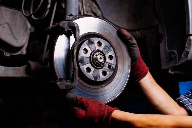 Hands in Red Gloves Holding a Car Brake Rotor — DK Mechanical Repairs in Warners Bay, NSW
