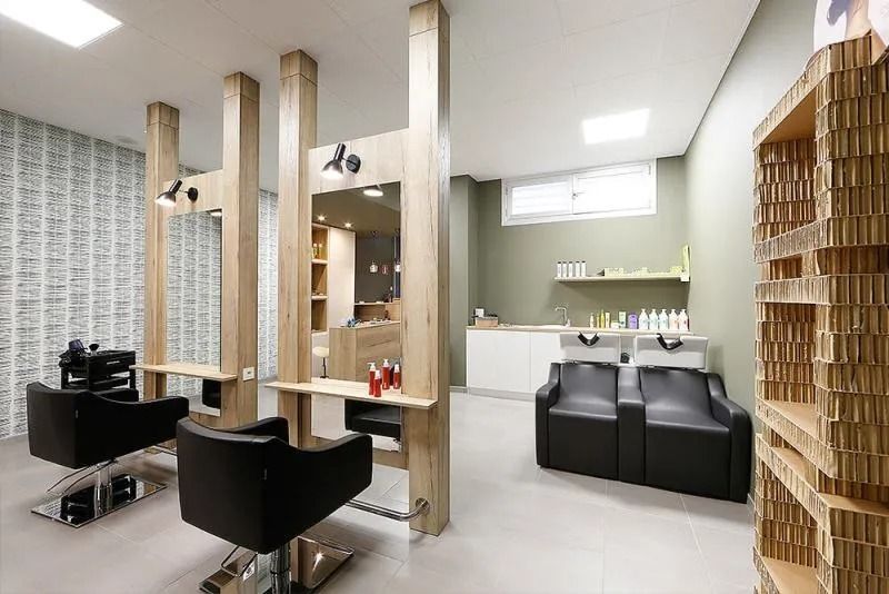 Interior de peluquería moderna con sillones de peluquería, espejos, estación de lavado de cabello y detalles en madera clara.