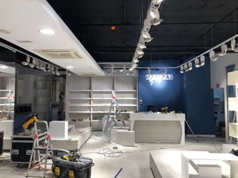 Interior de un local comercial vacío en obras, con escaleras, herramientas y una pared azul detrás de un mostrador.