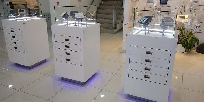 Tres pedestales de exhibición blancos con iluminación púrpura en una sala de exposición.