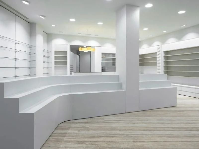 Interior vacío de una tienda minorista blanca con mostradores curvos y estantes en la pared.
