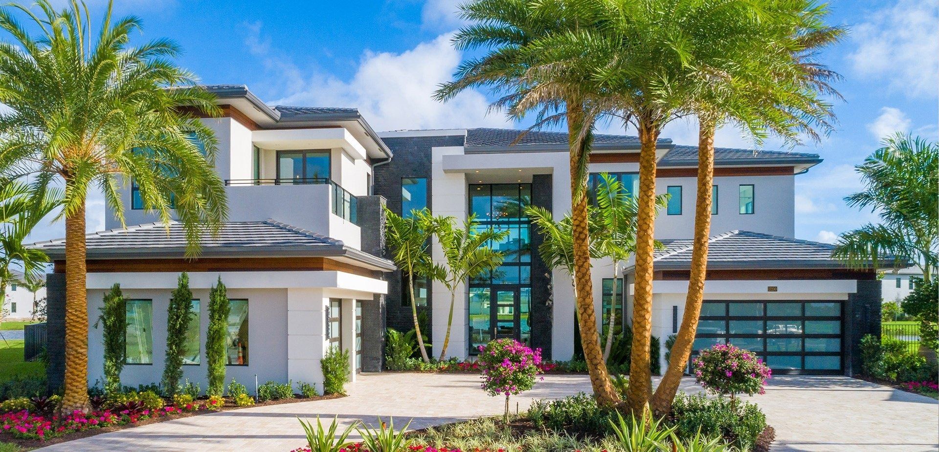 Modern white house with glass garage door, palm trees, and blue sky.