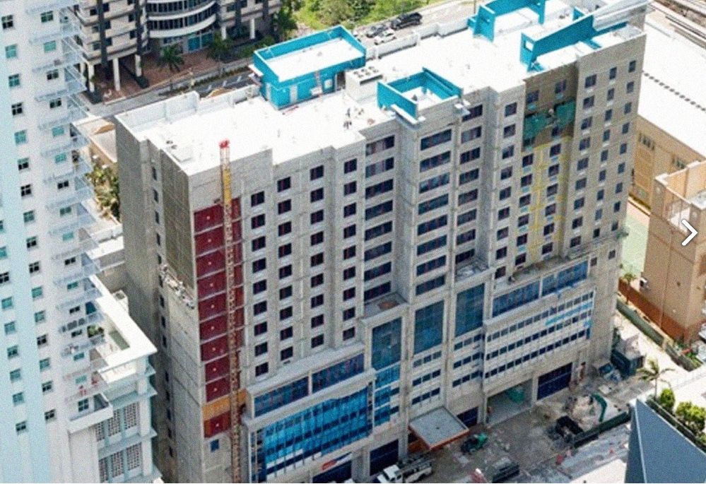 Aerial view of a multistory building under construction, with gray and blue exterior. A construction crane is visible.