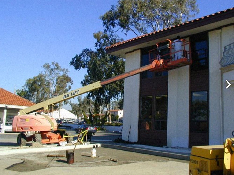 Man in orange lift working on the exterior of a building with dark-framed windows.