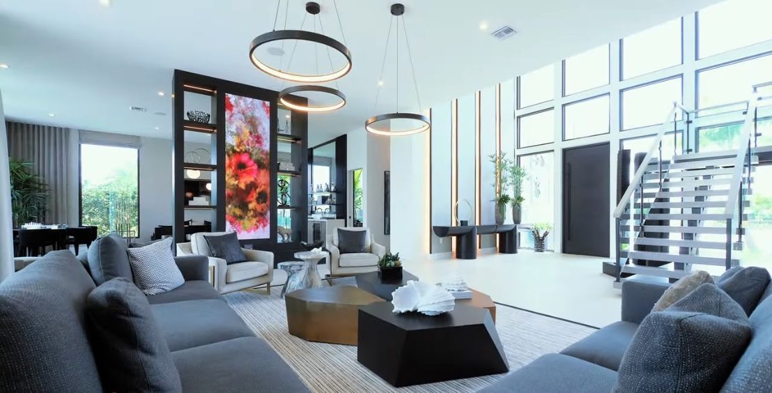 Spacious modern living room with gray furniture, decorative lighting, and a large display screen.