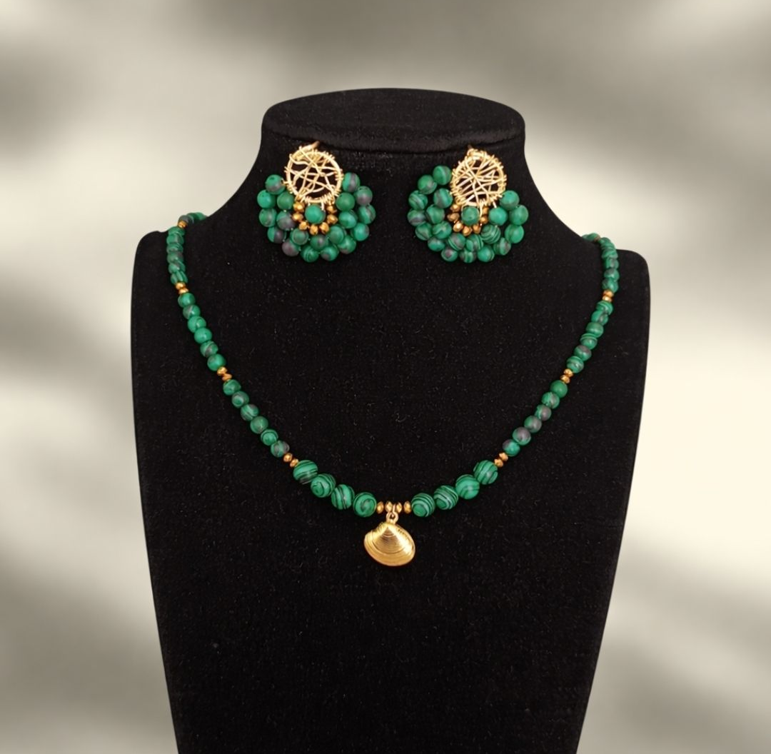 Un collar de cuentas verdes con un colgante central de concha marina dorada y pendientes redondos a juego con cuentas y detalles dorados.