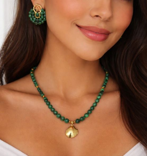 Una persona que lleva un collar de cuentas verdes con un colgante de concha dorada y pendientes de cuentas a juego.