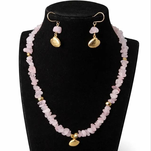 Un conjunto de collar y pendientes a juego, elaborados con fragmentos irregulares de cuarzo rosa y pequeñas cuentas de oro, presentados sobre una base negra.