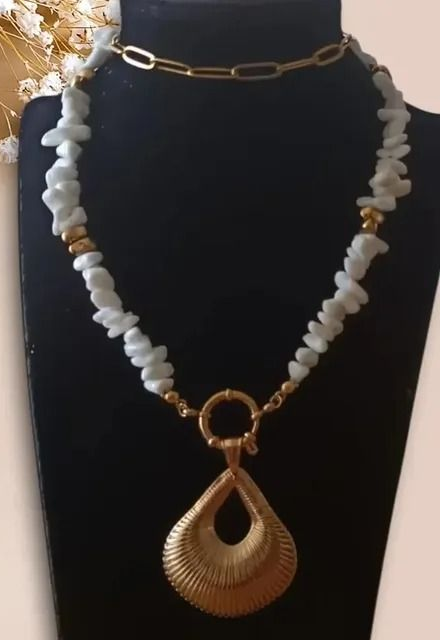 Un collar de cadena de oro y cuentas de piedra blanca con un gran colgante de oro texturizado en forma de lágrima sobre una base negra.