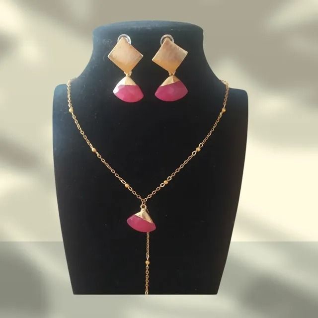 Un collar de cadena dorada y pendientes a juego con colgantes rosas en forma de abanico y detalles geométricos color canela sobre un busto negro.