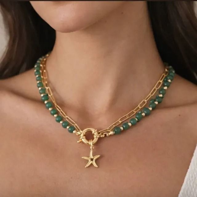 Un collar de oro en capas con cuentas verdes, una sección de eslabones de cadena, un cierre circular y un colgante de estrella de mar.