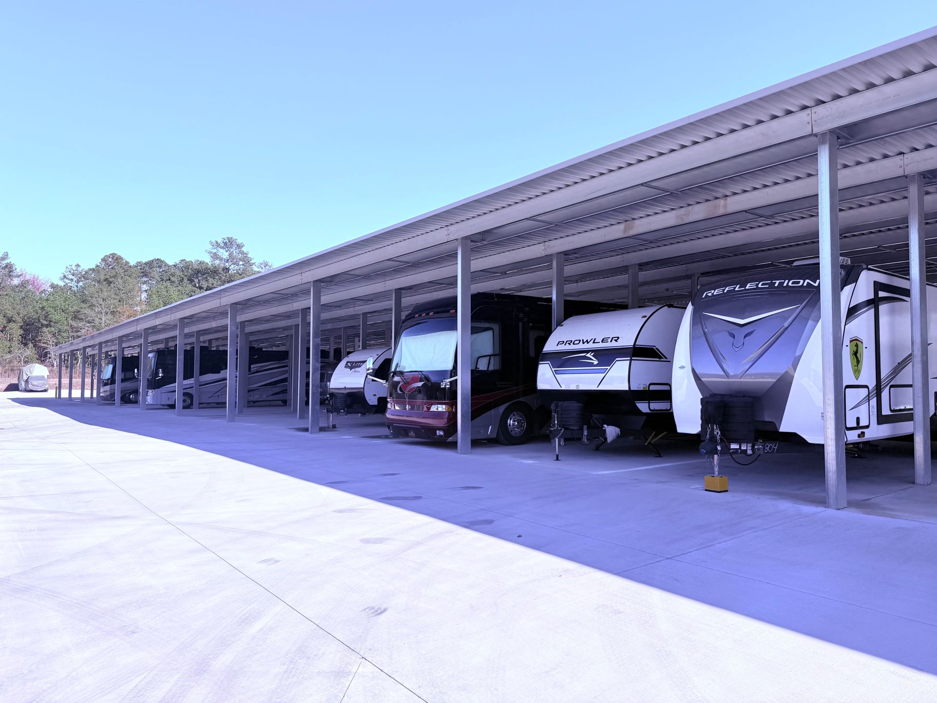 RV storage facility with multiple recreational vehicles parked under a long metal carport.