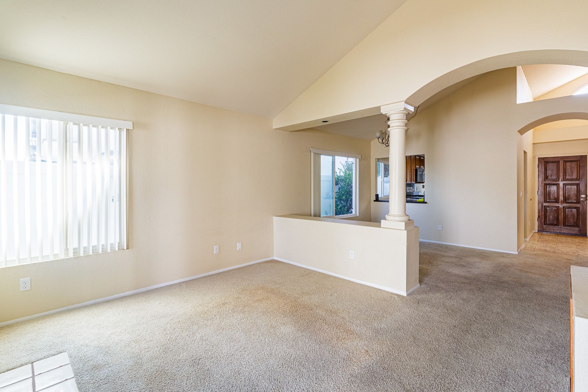 An empty living room with a vaulted ceiling and a carpeted floor.