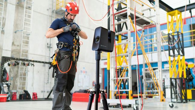 A man in a hard hat is standing in front of a tripod in a building.