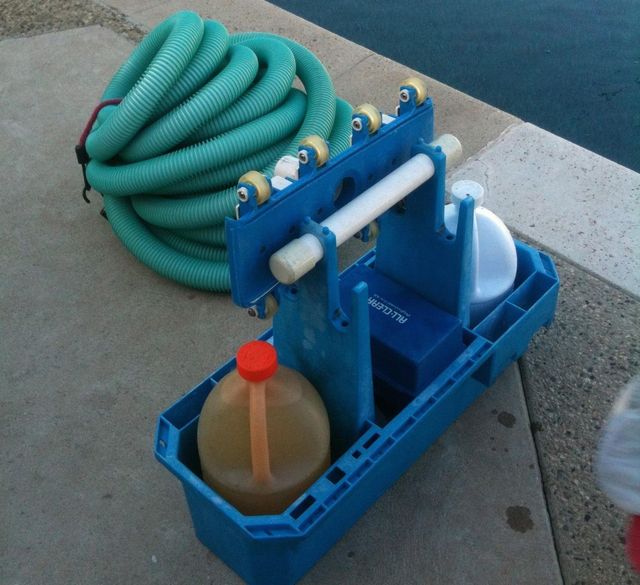 Blue pump with coiled green hose and brown container in a plastic tray on pavement