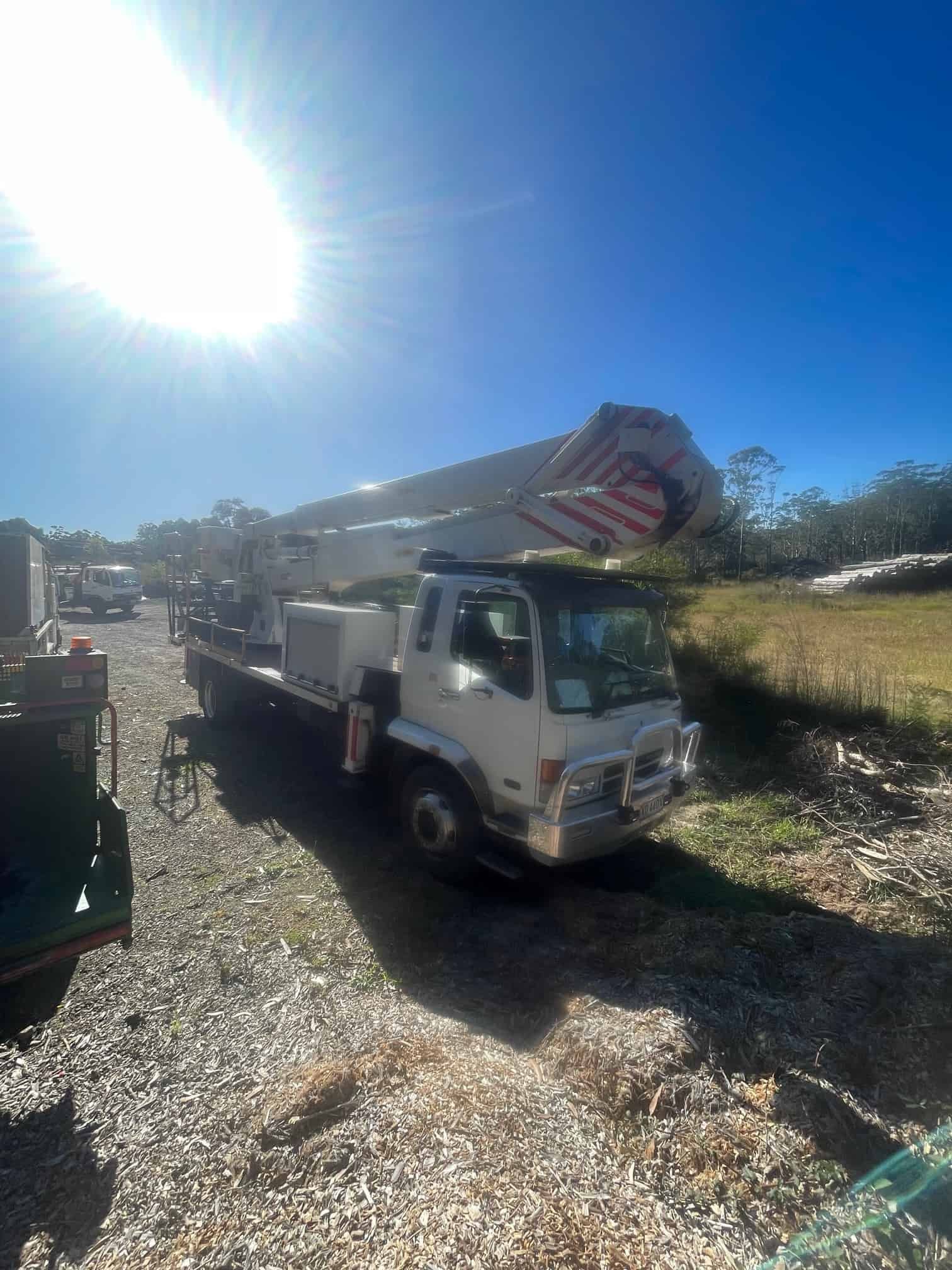 White Truck With A Crane On Top Parked In A Gravel Lot — Mike's Tree Services In Saint Georges Basin, NSW