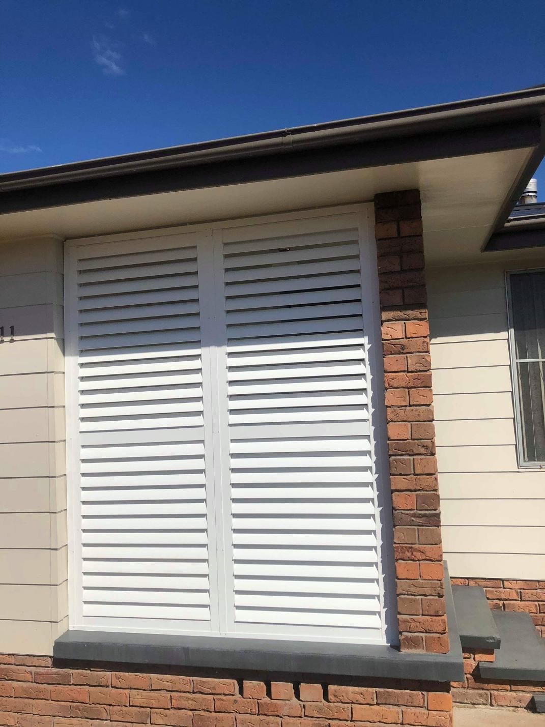 A House With White Shutters on the Windows and a Brick Wall — Design 2000 Blinds & Awnings In San Remo, NSW