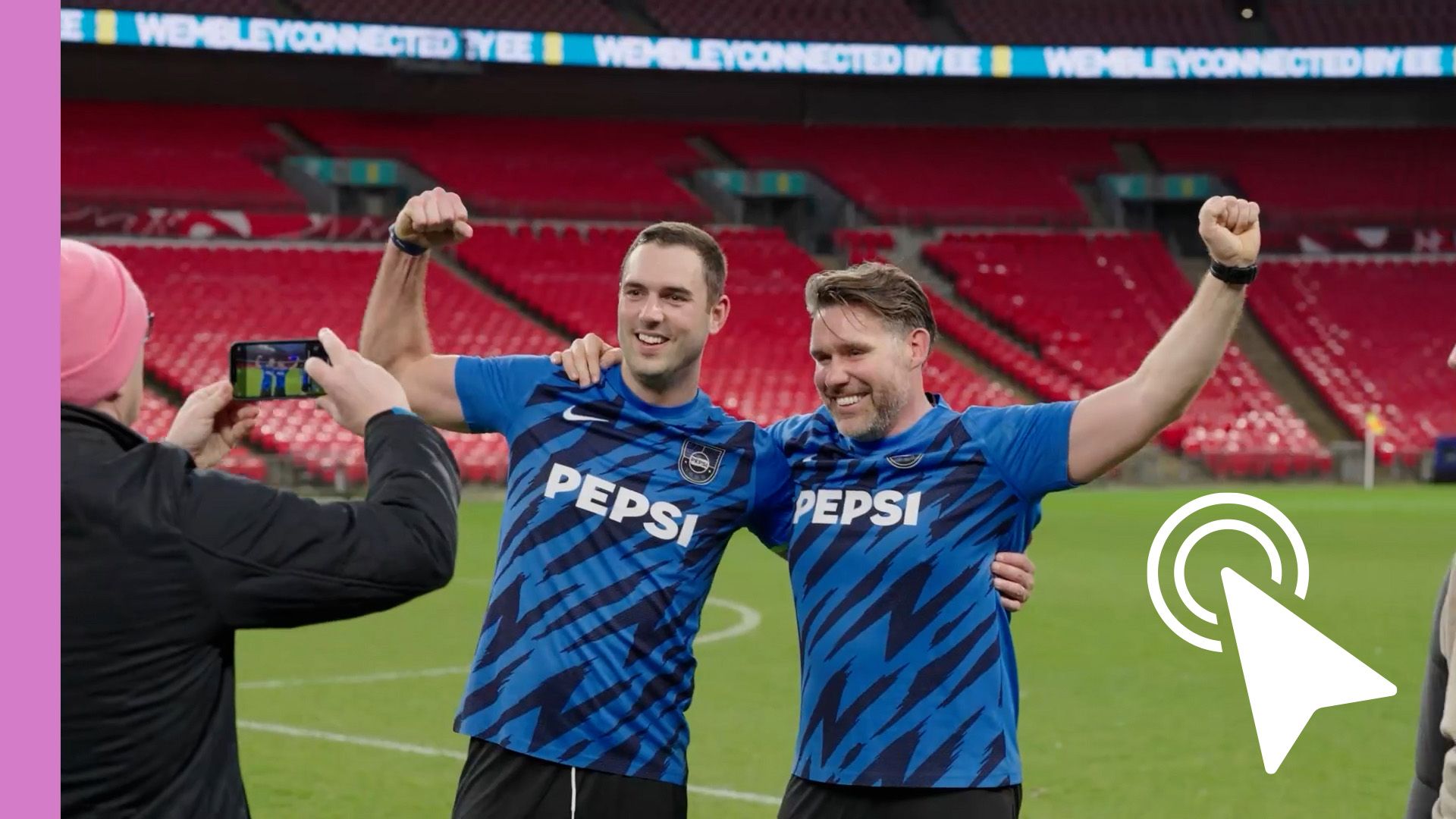 Two Pepsi-shirted athletes celebrate with raised arms on a stadium field as someone films them.