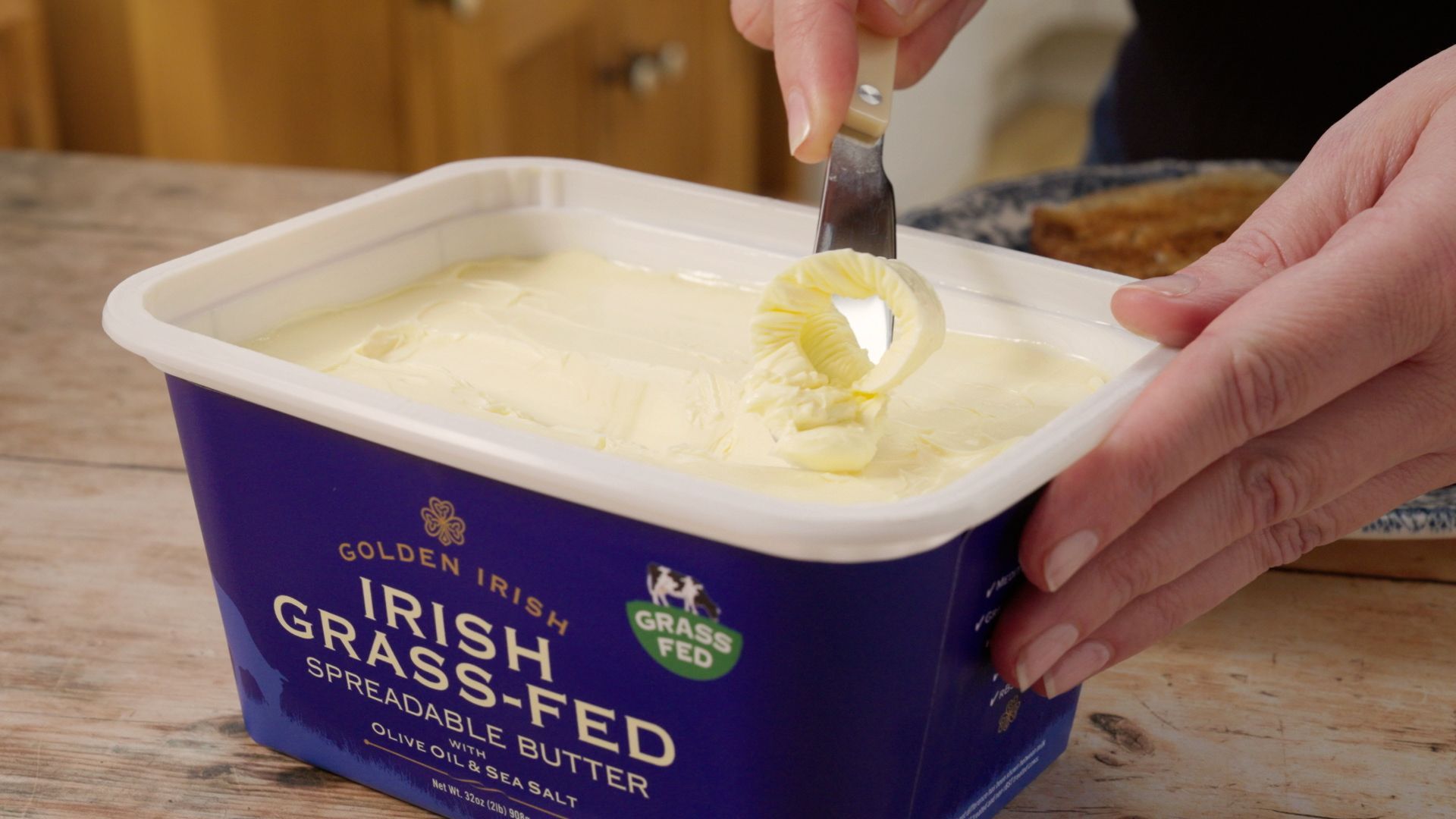 Hands scooping butter from a blue tub labeled “Irish grass-fed”