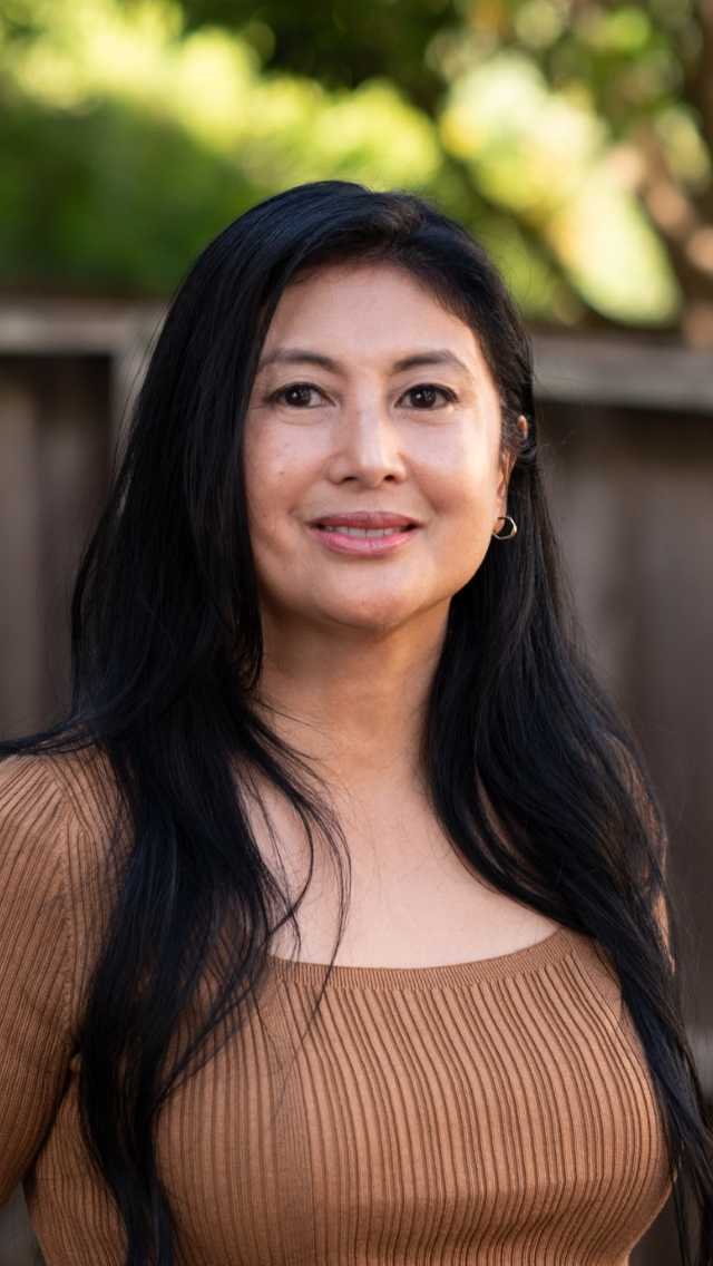 A woman with braids is wearing a blue jacket and smiling
