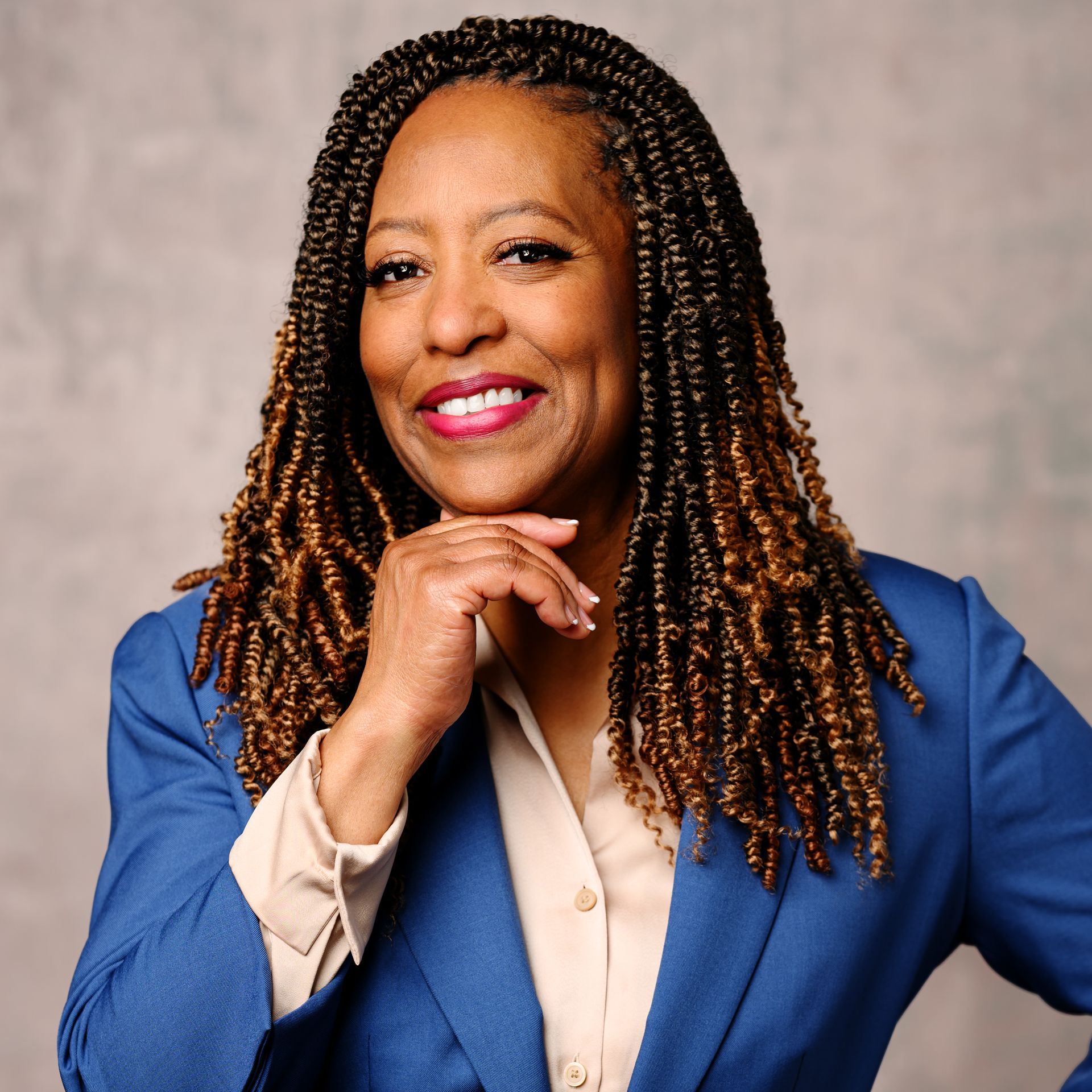 A woman with braids is wearing a blue jacket and smiling