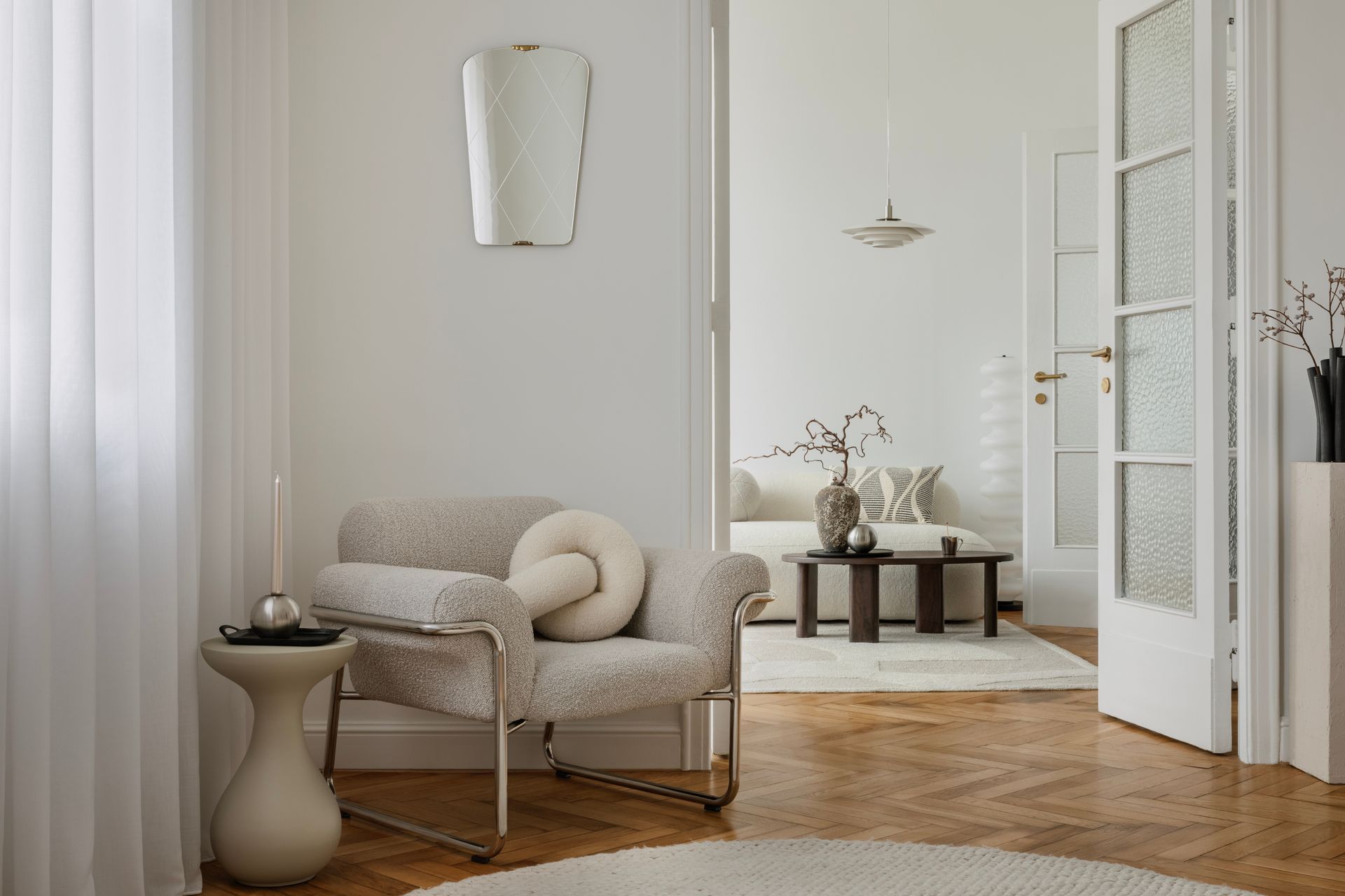 Cozy living room with a cream armchair, decorative mirror, and view into another room.