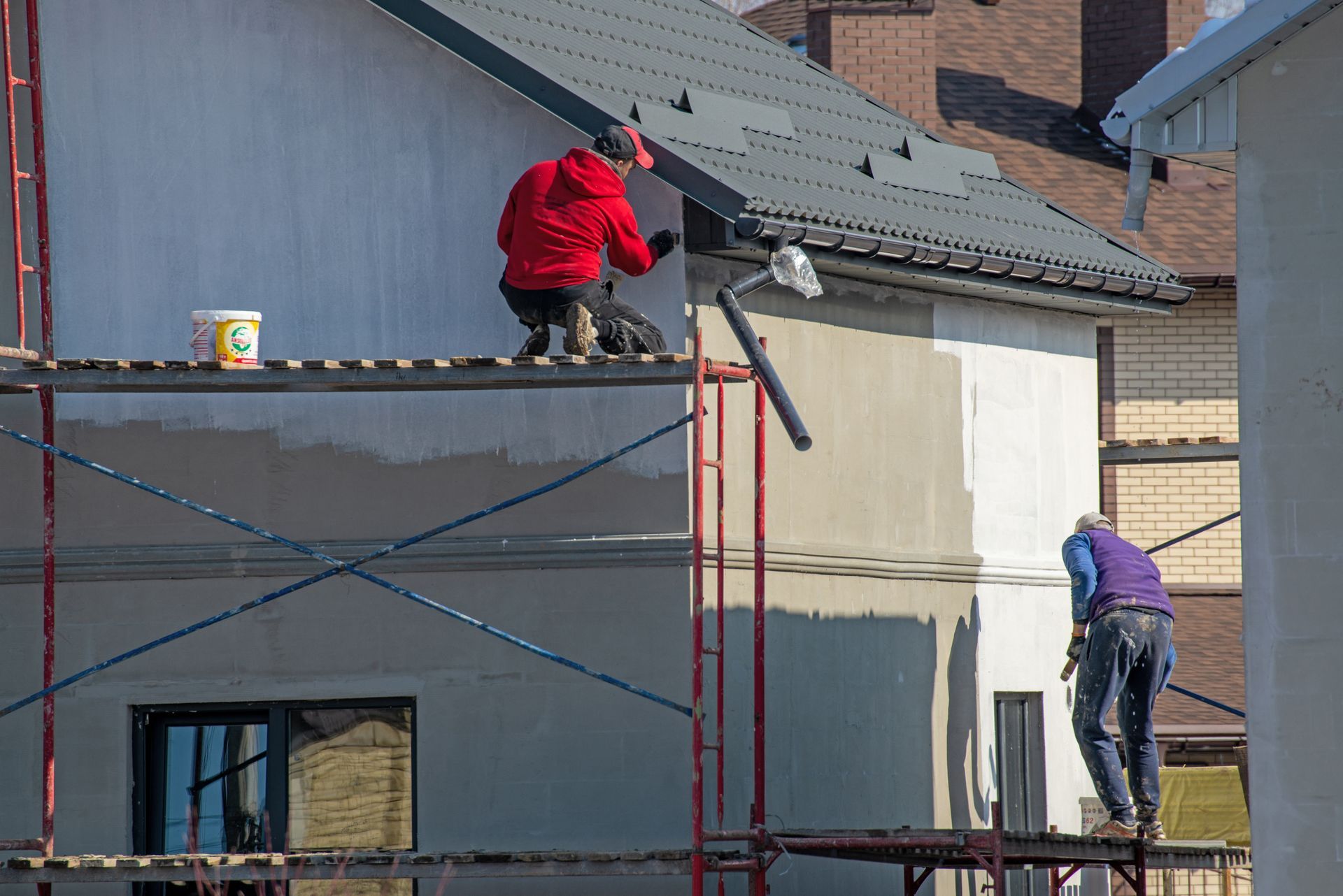 Two men are working on the roof of a house on scaffolding.