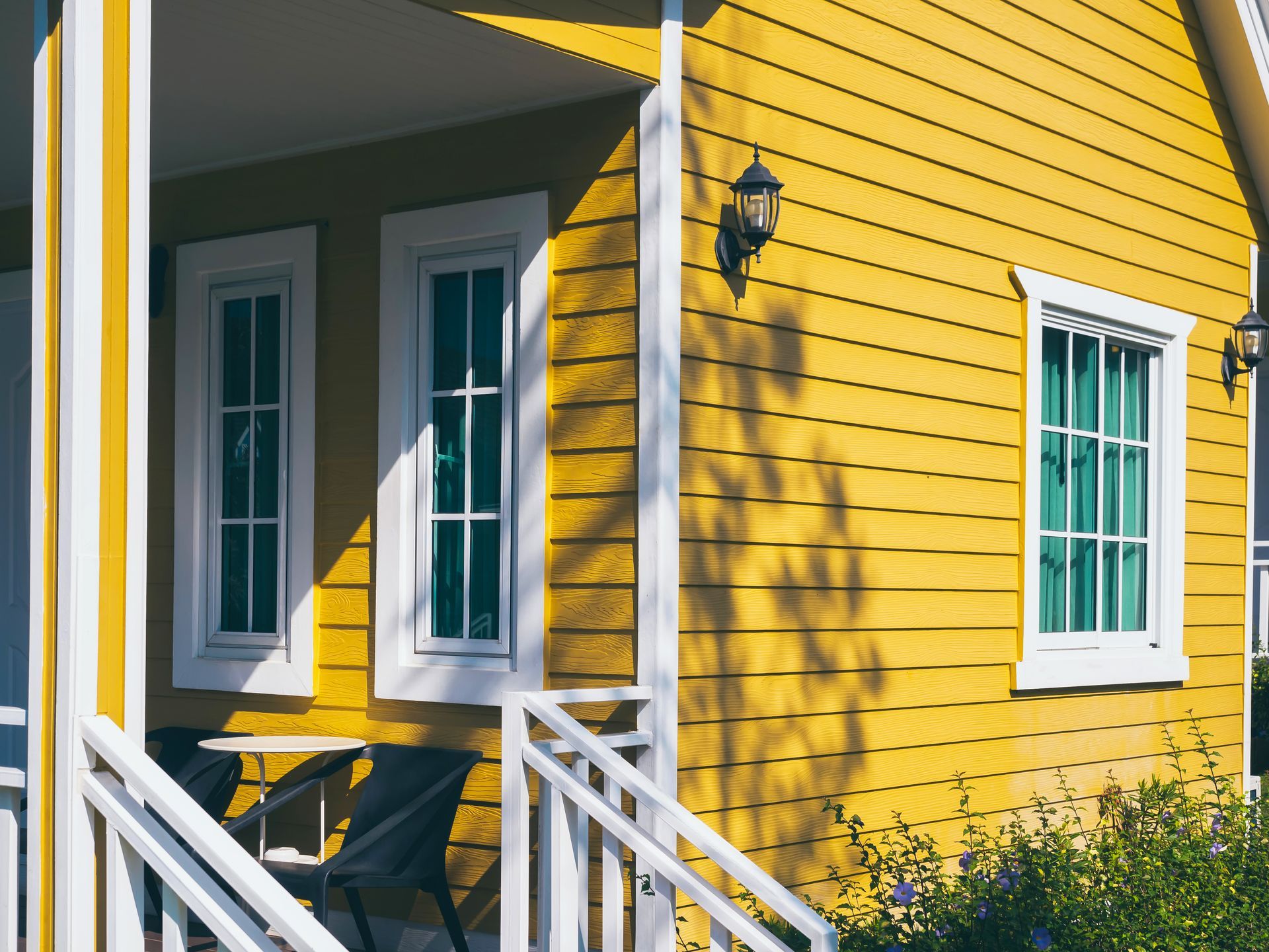 A yellow house with white trim and a porch with chairs and a table.